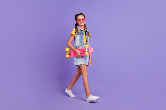 Full length photo of funny school blond girl go hold skate wear glasses t-shirt vest skirt shoes isolated on purple background