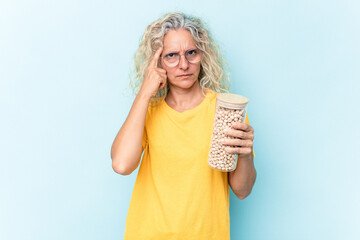 Middle age caucasian woman holding a chickpeas jar isolated on blue background pointing temple with finger, thinking, focused on a task.