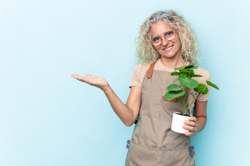 Middle age gardener woman holding a plant isolated on blue background showing a copy space on a...
