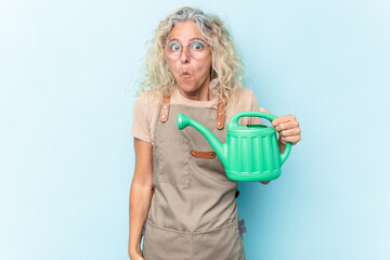 Obraz premium Middle age gardener woman holding a watering can isolated on white background shrugs shoulders and open eyes confused.