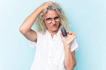 Middle age caucasian woman holding a car keys isolated on blue background being shocked, she has...