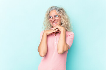 Middle age caucasian woman isolated on blue background keeps hands under chin, is looking happily aside.