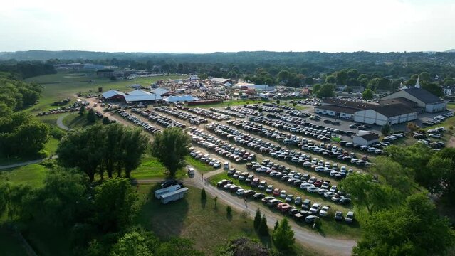 Aerial of many cars parked at outdoor fair festival during summer sunset. Busy public event venue.