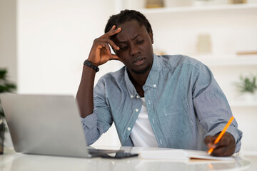 Naklejka premium Pensive Black Man Taking Notes While Working With Laptop At Home Office