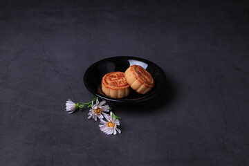 Chinese moon cake and the chrysanthemum is a symbol of autumn on a dark gray background. Asian traditional mid-autumn festival. Translation of hieroglyphs: mango, pomegranate and lotus.
