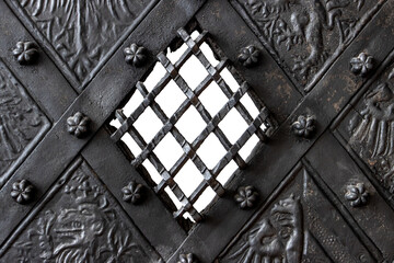 A medieval metal door with small window with grid, wrought and grooved, close up.