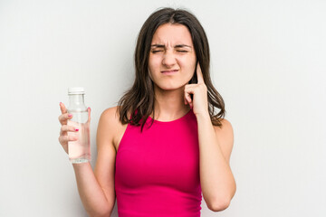 Young caucasian woman holding a bottle of water isolated on white background covering ears with hands.
