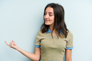 Young caucasian woman isolated on blue background pointing with finger at you as if inviting come closer.