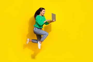 Full size photo of excited crazy girl jump run hurry hold use netbook isolated on yellow color background