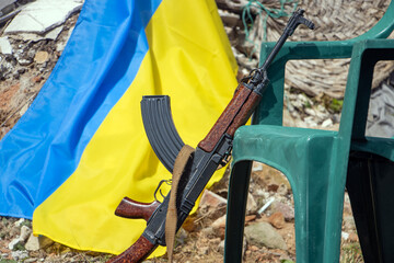 A machine gun leaning on a chair in front of ruins with a Ukrainian flag