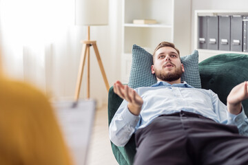 Bearded young man talking about strees and problems, psychologist consultation in bright office...