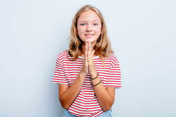 Caucasian teen girl isolated on blue background holding hands in pray near mouth, feels confident.