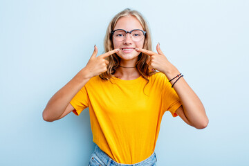 Caucasian teen girl isolated on blue background smiles, pointing fingers at mouth.