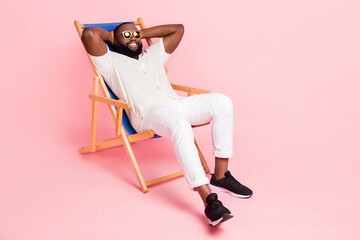 Photo of adorable funny guy dressed white shirt sitting deck chair arms behind head isolated pink...