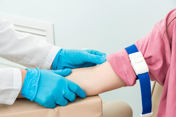 Cropped hands of nurse in blue gloves prepare patient's right hand for blood sampling procedure.