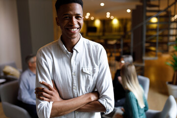 Portrait of a handsome casual businessman in office smiling while colleagues are having a meeting in background