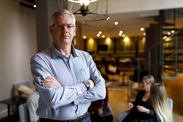 Portrait of a handsome casual businessman in office smiling while colleagues are having a meeting in background