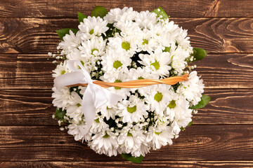 Fototapeta na wymiar Wicker basket of white chamomile chrysanthemums on wooden background. Gift flowers basket for the holiday