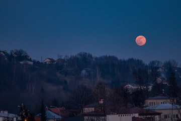 Red moon is rising above a hill. Dark blue colors and spectacular full moon