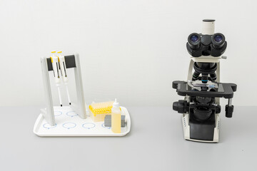 Medical microscope and board with instruments and test tubes are on gray table.