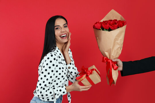 Happy Woman Receiving Tulip Bouquet From Man On Red Background. 8th Of March Celebration