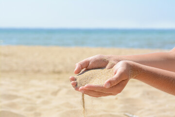Child pouring sand from hands on beach near sea, closeup with space for text. Fleeting time concept