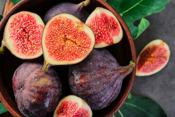 Fresh figs and fig halves on a brown old clay plate. Dark background, close-up top view. Seasonal ripe fruits, mediterranean diet