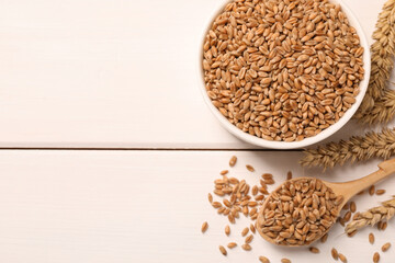 Wheat grains on white wooden table, flat lay. Space for text