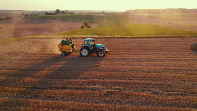 Golden field with bales of hay and blue tracktor stacking hay with green fields in the background. Agriculture. Horizontal shot. High quality 4k footage