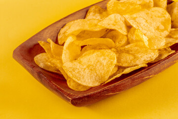Potato chips or crisps in a bowl and scattered on a yellow background, a close-up