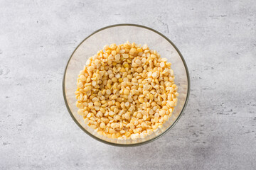 Glass bowl with soaked yellow peas on a gray textured background, top view. Cooking homemade vegan food