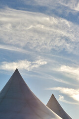Tent roofs against the blue sky and clouds. A row of white triangular pyramid marquee rooftops against a blue sky