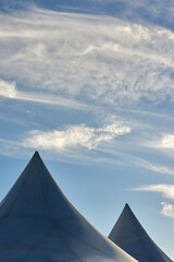 Tent roofs against the blue sky and clouds. A row of white triangular pyramid marquee rooftops against a blue sky