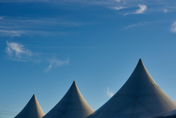 Tent roofs against the blue sky and clouds. A row of white triangular pyramid marquee rooftops against a blue sky