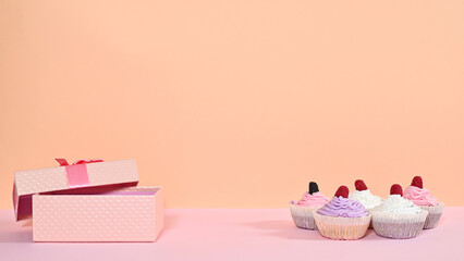 PAsastel pink gift and sweet cup cakes on pastel background for birthday