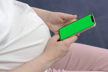 Pregnant woman holds mobile phone with green screen. Close-up. selective focus