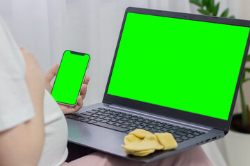 Phone and laptop green screen mockup. Pregnant woman looking at laptop and phone with chroma key.