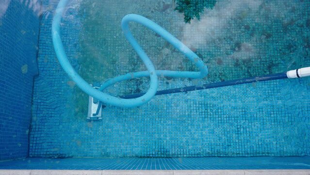 Cleaning process of dirty pool bottom with underwater vacuum. Blue tiles and clean water. 