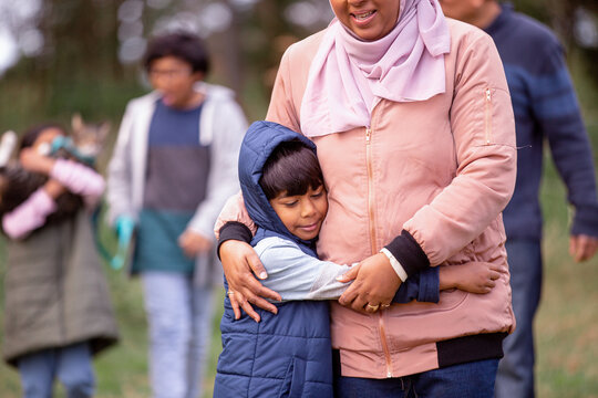 Close up shot of a boy wearing blue coat hugging a woman wearing pink sweater and hijab