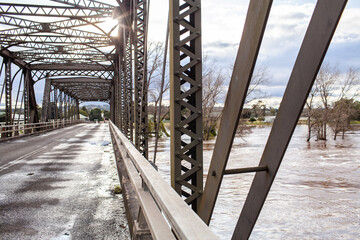 Brown floodwater seen through metal supports of old bridge during flood