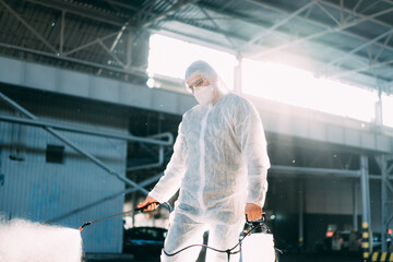 Man dressed white protective overalls spraying surface antibacterial sanitizer sprayer during...