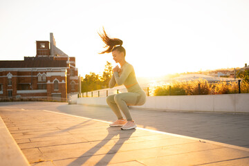 Sporty woman doing jumping squats exercises on stairs in park. Bodyweight training on sunset.
