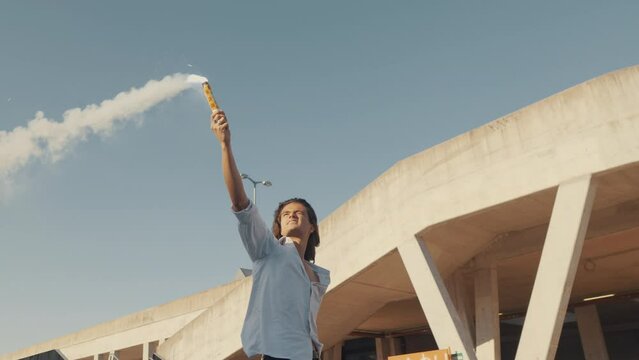 Teenager riding skate, holding burning flare in raised hand, freedom, youth, rebellion concept. Boy training for skateboarding performance, slow motion tracking shot, low angle view