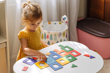 A little girl playing with wooden shape sorter toy on the table in playroom. Educational boards for...