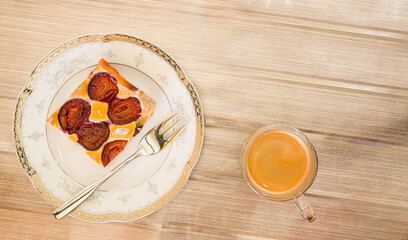 Portion of plum cake on a porcelain plate with a fork. A cup of espresso. View from above.