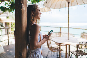 Positive woman browsing mobile phone in tropical resort