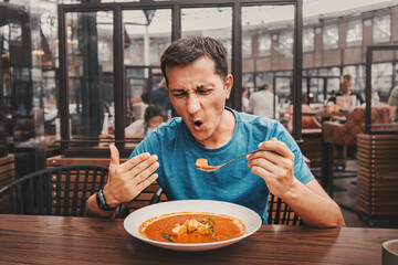 A man tries a spicy and hot red soup in a restaurant and reacts funny emotionally. Seasonings in...