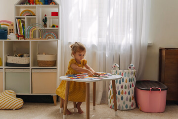 A little girl playing with wooden shape sorter toy on the table in playroom. Educational boards for Color and Shapes sorting for toddler. Learning through play. Developing Montessori activities.