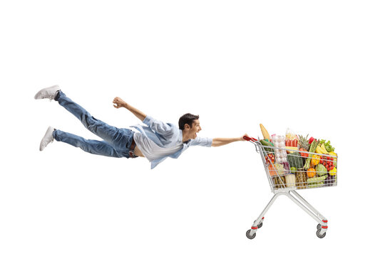 Full length shot of a casual young man flying and holding a shopping cart with food