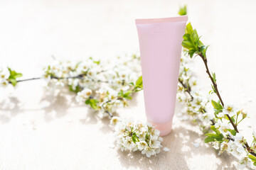 One white blank cosmetic tube bottle and flower, blooming branch on pink background. Natural Organic Spa Cosmetic Beauty Concept. Mockup Front view.